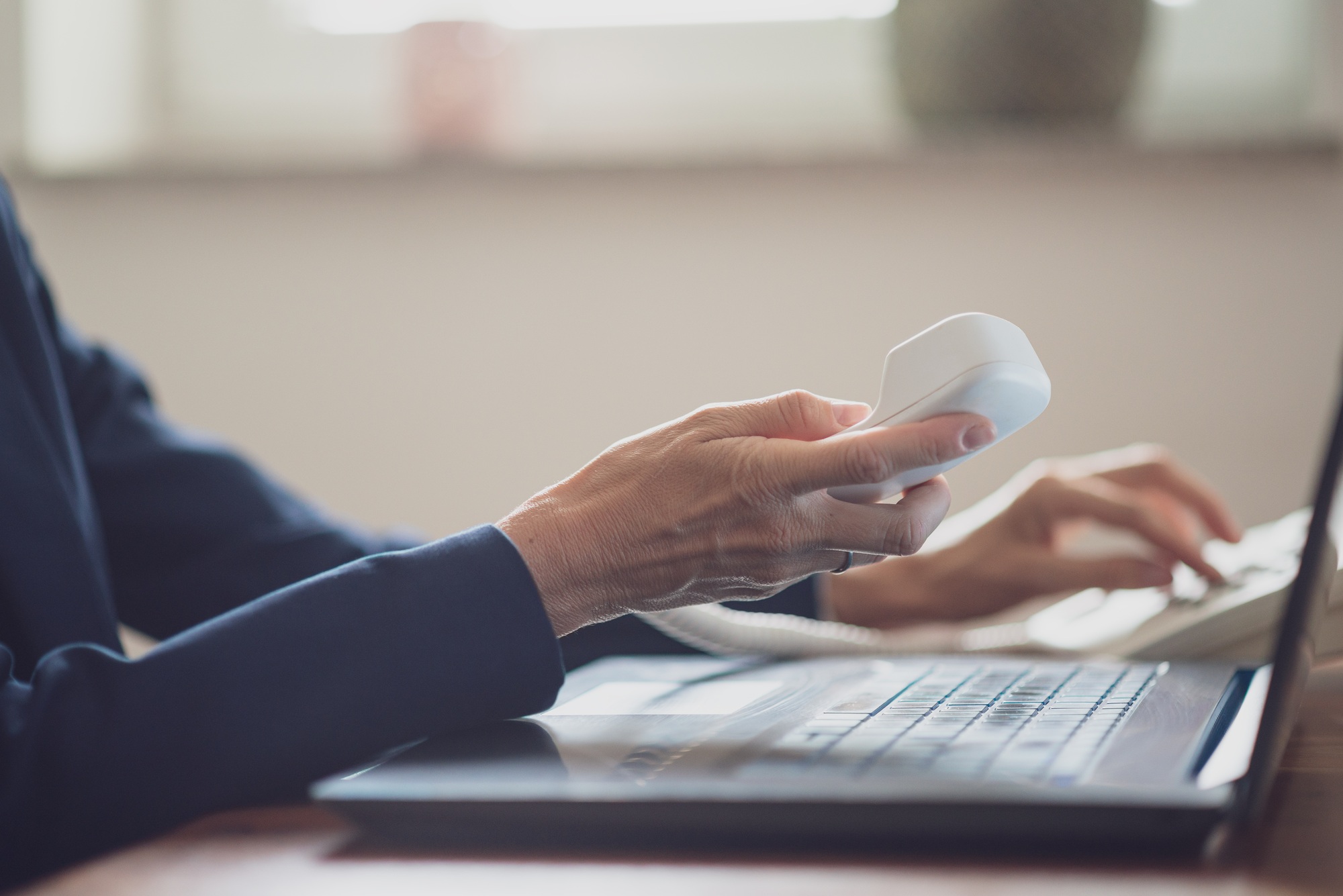 Female business assistant holding white landline phone handset dialing a telephone number